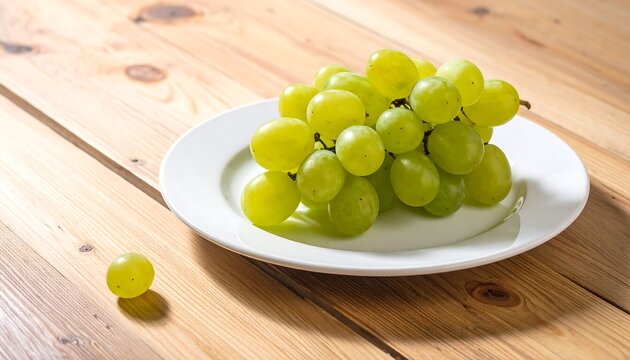 A close-up shot of green grapes on a white plate atop a light-colored wooden table. One grape is separate