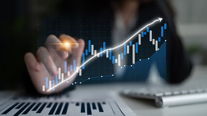 A business professional interacts with a digital graph showing stock market trends, highlighting growth and analysis in a modern office setting. Impute