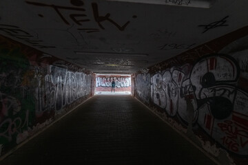 Young woman with long dark hair wearing a black coat stands confidently in front of a vibrant graffiti wall, showcasing urban fashion and self-expression in a contemporary setting