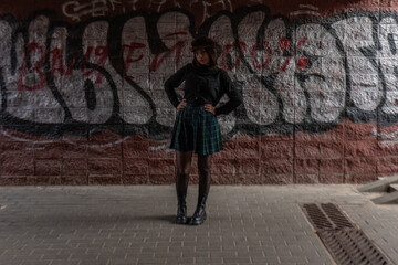 Young woman with long dark hair wearing a black coat stands confidently in front of a vibrant graffiti wall, showcasing urban fashion and self-expression in a contemporary setting