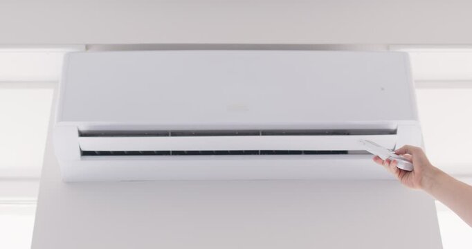 Close up of a man hand using a remote control to turn on the air conditioner at home. Using remote control to adjusts the climate condition, ensuring a comfortable indoor environment.