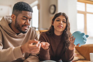 Young couple budgeting together with piggy bank at home in cozy setting