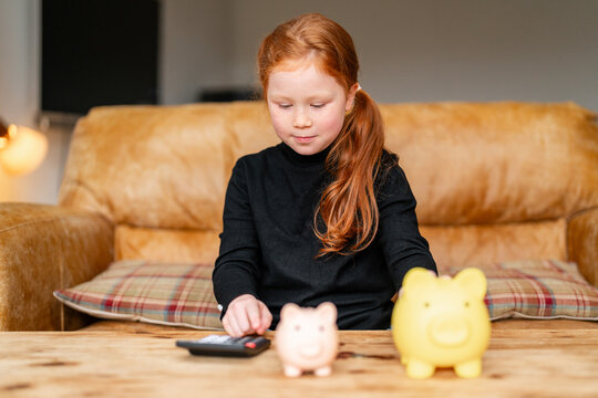 Child counting savings using piggy banks at home in cozy living room