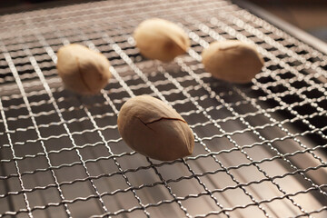 Several dry pecan nuts roasting on a metal grill mesh, close-up, natural texture and lighting, food photography