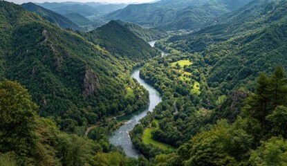 High-angle view of a winding river carving through a lush valley, surrounded by steep, forested mountains