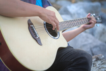 Close-up of hands playing an acoustic guitar outdoors, musician strumming strings with natural bokeh background