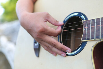 Fototapeta premium Close-up of hands playing an acoustic guitar outdoors, musician strumming strings with natural bokeh background