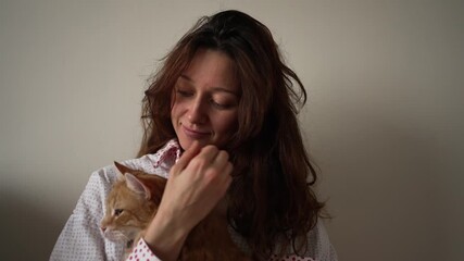 Compassionate woman gently cuddling her cute orange kitten in the comfort of her home. This pet owner is showering her furry friend with love and care, savoring a tranquil moment together inside