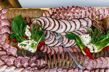 Charcuterie board with sliced meats and greens. Top view of an elaborate charcuterie platter featuring assorted cured meats, sausages, leafy greens, mushrooms, and red chili peppers.