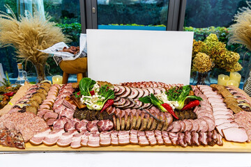 Large charcuterie board with assorted cured meats. An elaborate charcuterie spread featuring a wide variety of sliced meats, sausages, herbs, and garnishes arranged on a wooden board.