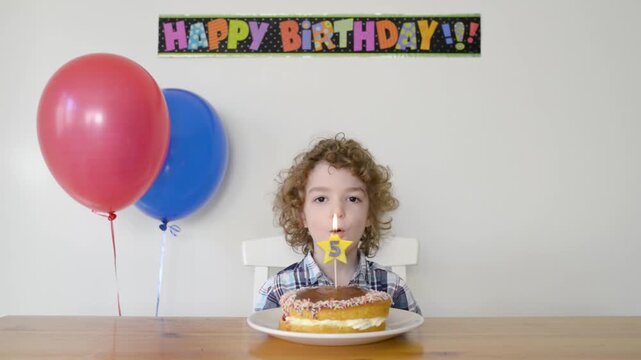 Young boy celebrating his fifth birthday at home blowing out a candle on his birthday cake