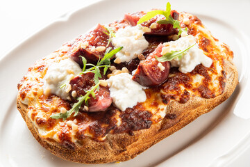  savory-sweet fig and cheese bruschetta appetizer on a white rectangular plate, featuring rich golden-brown melted cheese, fresh figs, and arugula garnish.