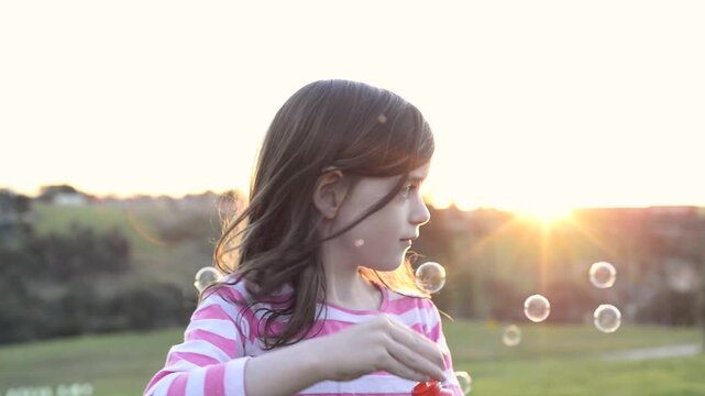 Happy young girl blowing soap bubbles in the park at sunset