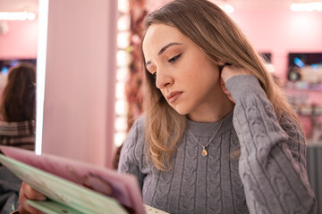 Young woman reading a menu in a cozy cafe with pink decor during afternoon hours