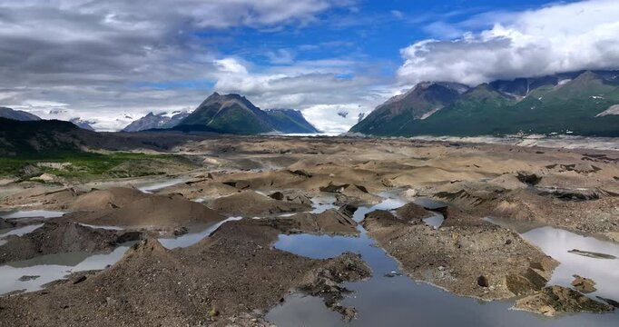 Glacial moraine landscape in Alaska. Pools of meltwater dot a gray moraine plain stretching toward distant Alaska glaciers.