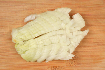 A small, irregular pile of freshly diced white onion pieces is centered on a light brown bamboo or wooden cutting board