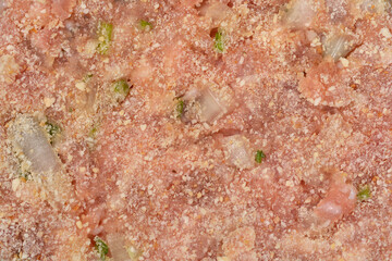 An extreme close-up shot of a raw, seasoned ground meat patty coated in a layer of fine breadcrumbs, showing chunks of onion and herbs