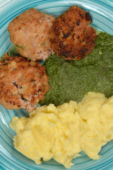 A vertical close-up of a portion of a meal featuring three fried meat patties, creamy mashed potatoes, and green pureed spinach on a blue plate