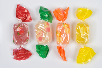 A horizontal line of four individually wrapped fruit-flavored jelly candies, showing red, green,...