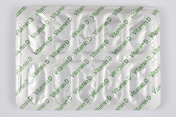 A full silver foil blister pack clearly labeled with "Vitamin D" in green text is centered and shown from an overhead perspective on a simple light gray background