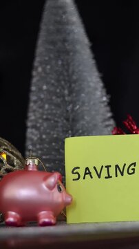 Varios adornos navide&ntilde;os y un cerdo de color rosado rodeados de luces de colores con una nota con la palabra ahorro, pera celebrar la navidad feliz. Video vertical