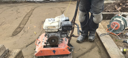 Worker operating a compactor machine on a construction site to prepare a surface for paving or concrete work