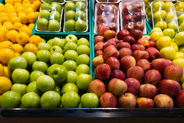 Vibrant Display of Fresh Apples (Red, Green, and Yellow Varieties) and Oranges Neatly Arranged in Crates and Plastic Trays in a Modern Supermarket Produce Section.