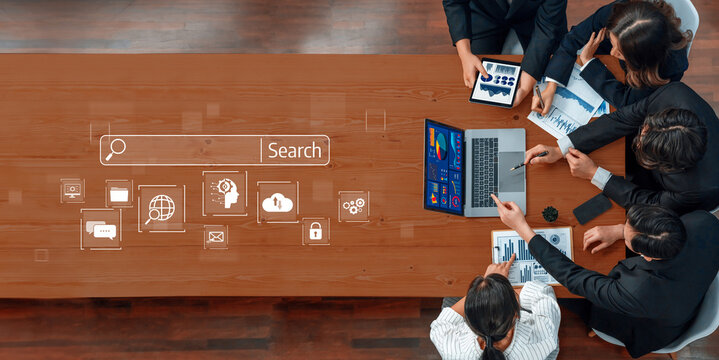 A diverse business team engaged in a collaborative meeting around a wooden table, analyzing digital data charts and utilizing various electronic devices for effective teamwork. Trope