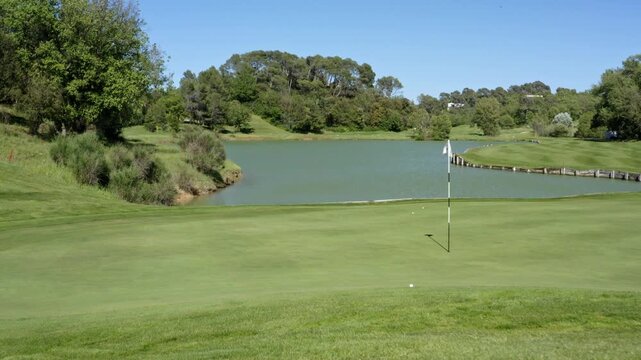 Golfer swings on sunny day at picturesque golf course near lake