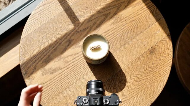Top-down flatlay video footage of a photographer holding a coffee cup above a camera on a wooden table, symbolizing creativity, lifestyle, and warm cafe atmosphere.
