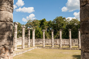 Exploring ancient Mayan city ruins, stone columns rise from the grassy ground, showcasing the historical architecture and archaeological site under a vibrant blue sky in Chichen Itza, Mexico