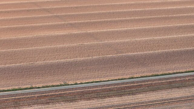 Aerial view displaying tilled agricultural fields in Italy's Po Valley during late summer, with distinct soil furrows creating a striped pattern ready for new crops slow motion