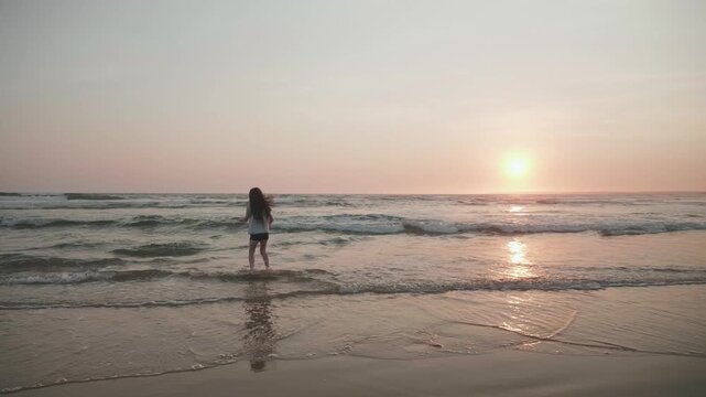 Happy young girl playing at the beach having fun  jumping over waves at sunset; Melbourne, Victoria, Australia