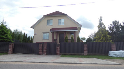 Two-story house with garden and fence located on a quiet street under cloudy sky