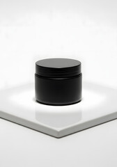 A close-up shot of a small, matte black jar with a screw-on lid, sitting on a white surface.