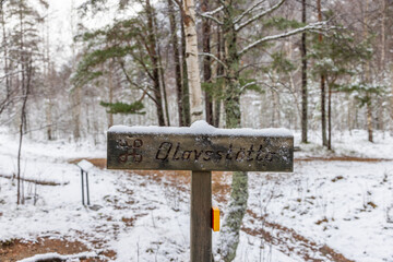 Naklejka premium A tall stone marker stands in the snowy forest, surrounded by pine trees and distant mountains, the metal cross atop it rising quietly into the winter sky. location Olavsstøtta in Norway.