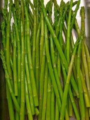 Fototapeta premium A vertical, close-up shot of a bunch of bright green, cooked or blanched asparagus spears lying in a shiny metal tray.