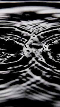 Dramatic slow motion close up of symmetrical water ripples spreading outward across a glossy dark liquid surface creating an echo effect fluid, concept, symmetrical water ripples