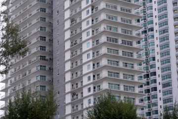 Naklejka premium A modern, multi-story apartment building with numerous balconies and windows stands tall amidst green trees, showcasing contemporary urban architecture and residential living
