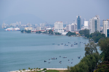 Fototapeta premium Fishing boats rest along the blue waters of Gurney Bay in Penang, framed by modern high-rise buildings and a scenic coastal view.