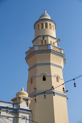 Obraz premium Lebuh Acheh Mosque in Georgetown, Penang, Malaysia with yellow minaret and Islamic architecture under clear blue sky. 