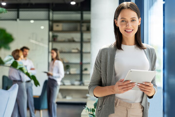 Obraz premium Young elegant business woman standing with digital tablet near office window