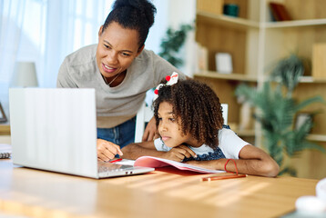 Mother and daughter doing homework with laptop at home. Mom, dad and teenage black girl happy using laptop. Teen girl and parents sitting at home working with notebook