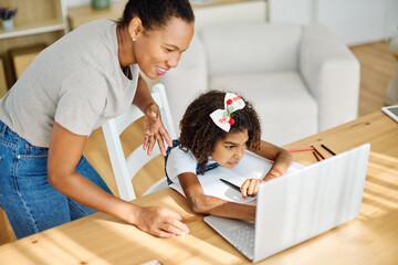 Mother and daughter doing homework with laptop at home. Mom, dad and teenage black girl happy using laptop. Teen girl and parents sitting at home working with notebook