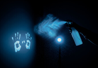Forensic scientist in a dark room spraying luminol reagent to reveal invisible bloodstains on a wall which glow with blue chemiluminescence crime scene investigation concept