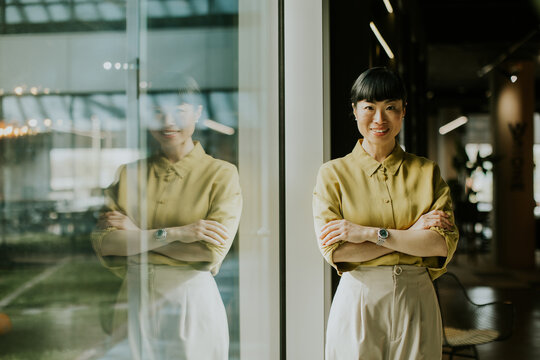Confident woman stands by window in modern workspace during daylight