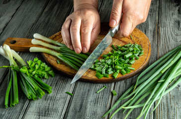 Hands are skillfully chopping fresh green onions on a wooden cutting board. The scene shows vibrant vegetables and kitchen tools, highlighting the act of preparing ingredients for cooking