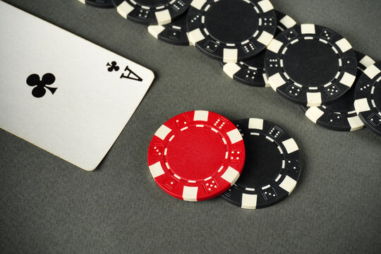 A red poker chip and black chips surrounding an ace of clubs on a gray table surface indicate a thrilling card game. Players are focused, enjoying their time