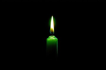 A green candle burns brightly with a warm, vivid flame against a stark, dark backdrop