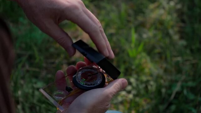 close-up view traveler hands opening professional sighting compass and turning the bezel to find right direction, with natural green background for outdoor exploration.